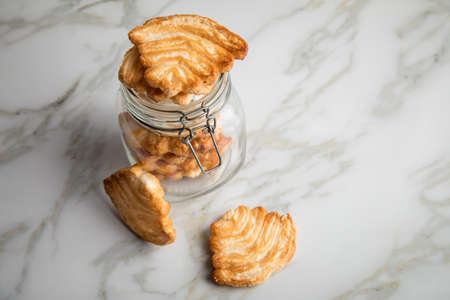 Italian puff pastry fan wavers cookies biscuits with preserving glass jar on marble table backgroundの写真素材