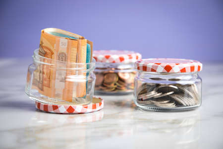3 glass jars with Euro notes, 2â¬ coins and loose cash for housekeeping and savingsの写真素材