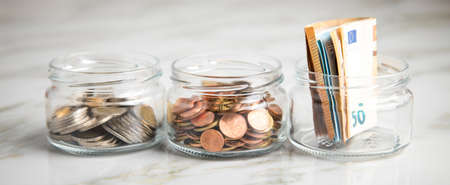3 glass jars with Euro notes, 2â¬ coins and loose cash for housekeeping and savingsの写真素材
