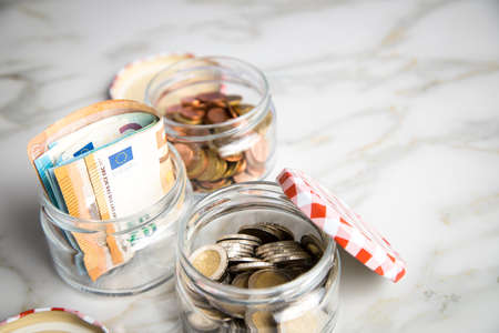 3 glass jars with Euro notes, 2â¬ coins and loose cash for housekeeping and savingsの写真素材