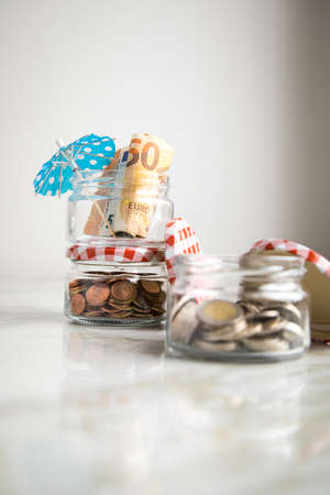 3 glass jars with Euro notes, sunshade, 2â¬ coins and loose cash for housekeeping and vacation savingsの写真素材