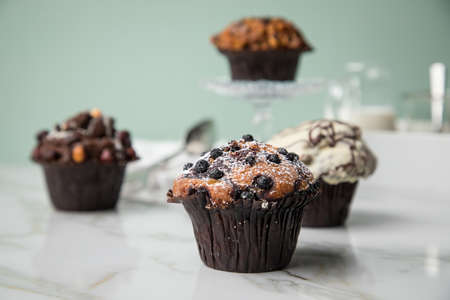 Muffin selection with blueberry, walnuts, hazelnuts and white chocolate with milk and sugar for coffee break on marble table and green backgroundの写真素材