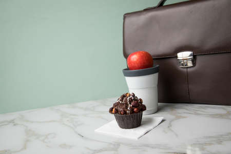 Hazelnut muffin, coffee in to go mug and apple as breakfast on the way to work with leather briefcase on marble table and green backgroundの写真素材