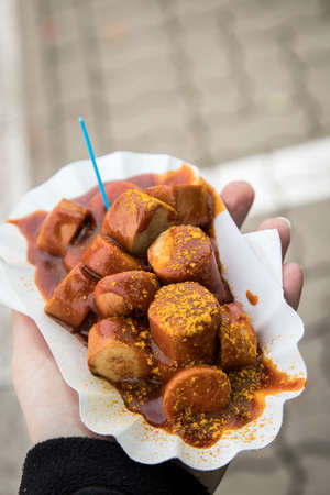 Woman eating typical German Currywurst street food is grilled and sliced sausage with curry ketchup in paper plate on the goの写真素材