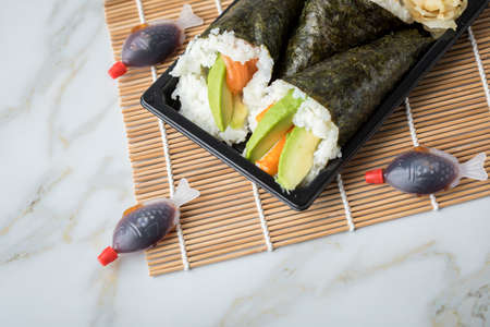 Salmon and Surimi avocado Temaki sushi with soy sauce fish, pickled ginger and wasabi in take away Bento box on mat and marble backgroundの写真素材