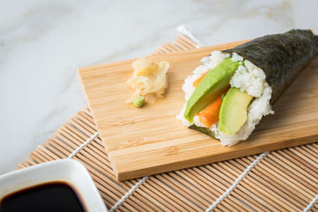 Surimi avocado Temaki sushi with soy sauce, pickled ginger and wasabi on mat, bamboo tray board and marble backgroundの写真素材