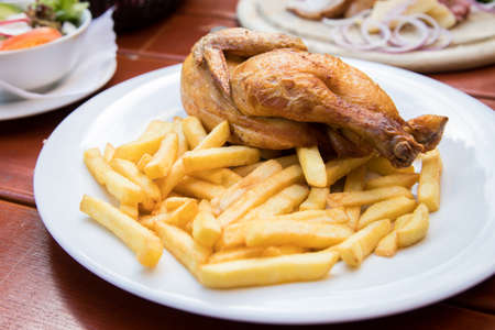 Roasted chicken half with French fries on porcelain plate outdoors in German beer garden