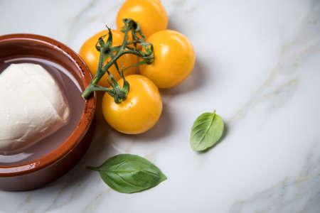 Yellow tomatoes with mozzarella cheese and basil on marble background