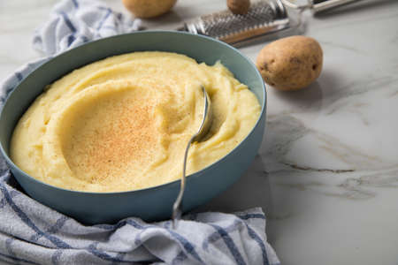 Bowl with mashed potatoes and ingredients as potato, nutmeg with kitchen towel and grinder on light...