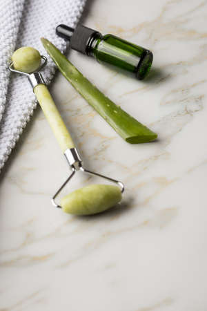 Massage stone roller, Aloe Vera leaf and green natural organic beauty face oil serum bottle for cosmetic treatment skin care with towel and marble backgroundの写真素材