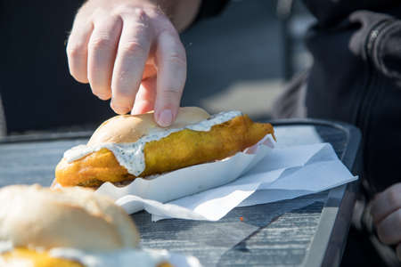 Man eating typical German Friesland deep fried Pollack fish in beer batter as bread bun roll with sauce tartar on wooden tableの写真素材