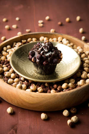 Hazelnut muffin in golden metal bowl on nuts and wooden table background