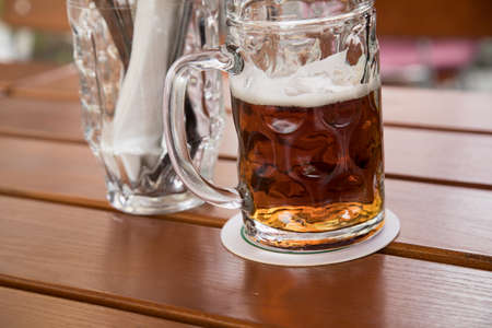 Glass dark German Vollbier beer in beer garden during summer on wooden table backgroundの写真素材