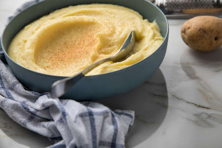 Bowl with mashed potatoes and ingredients as potato, nutmeg with kitchen towel and grinder on light...