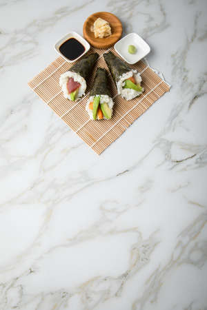 Salmon, tuna fish and Surimi avocado Temaki sushi with soy sauce, pickled ginger and wasabi on mat and marble backgroundの写真素材