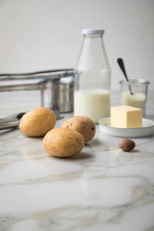 Potato, milk, salt, butter, nutmeg as ingredients with press and grinder for mashed potatoes on light marble backgroundの写真素材