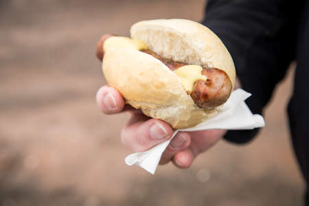 Man eating typical grilled German Bratwurst sausage street food with bread roll bun and mustard on the goの写真素材