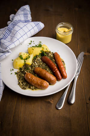Traditional German Oldenburger green cabbage with smoked pork sausage mix, mustard and boiled potatoes on wooden tableの写真素材