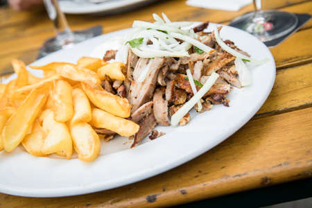 Greek pork meat Gyros with onions, Tsatsiki and French fries on wooden table in restaurant