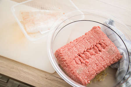 Mixed minced meat of pork and beef from plastic tray packaging in bowl on cutting board for cooking...