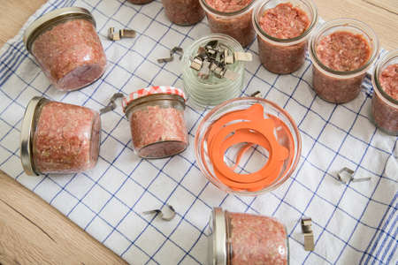 Raw mixed minced meat with pork and beef in screw-cap and preserving mason glass jars on towel for self-made pressure canning in domestic kitchen for long term food storage in pantryの写真素材