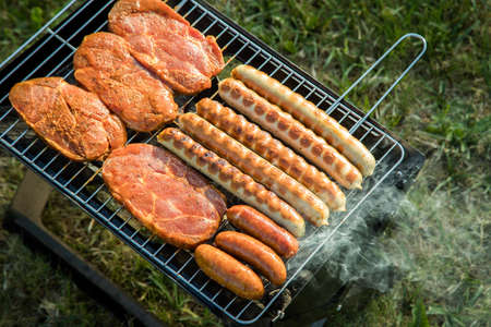 German Bratwurst sausages and marinated pork neck steak meat roasting with smoke on foldable...