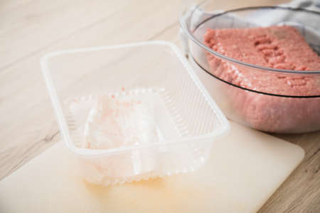 Mixed minced meat of pork and beef from plastic tray packaging in bowl on cutting board for cooking in domestic kitchenの写真素材