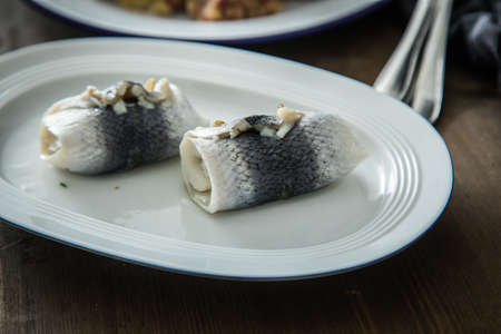 2 German Rollmops rolled pickled herring with gherkin onion filling on porcelain plate with cutlery,...