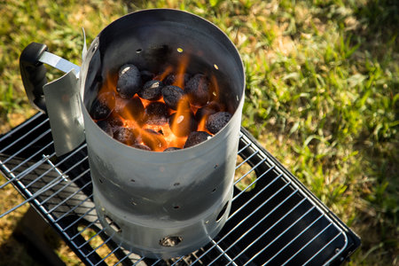 Coal of charcoal grill burning in flames with fire and lighter in barbecue chimney for BBQ eveningの写真素材