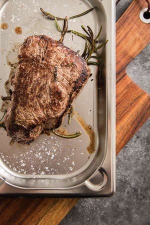 Medium rare fried beef steak with rosemary and salt on stainless steel tray, wooden board and dark stone backgroundの写真素材