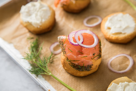 Gravlax a raw, marinated graved salmon with dill on bred roll bun with cream cheese, onion rings on tray with baking paper and light marble backgroundの写真素材