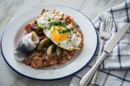 North German Hamburg Labskaus is a delicacy with corned beef, potatoes, beetroot, pickled gherkins, fried egg and herring on enamel plateの写真素材