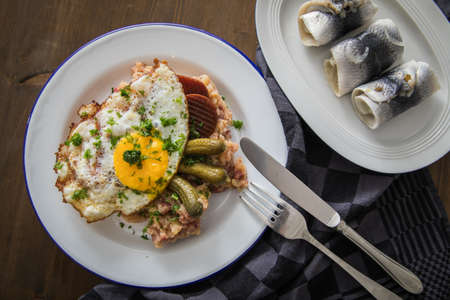 North German Hamburg Labskaus is a delicacy with corned beef, potatoes, beetroot, pickled gherkins, fried egg and herring on enamel plateの写真素材