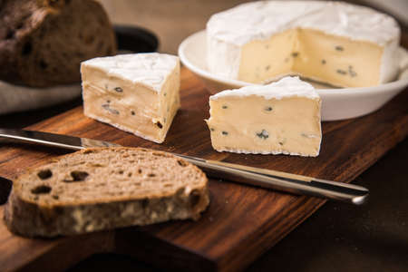 Loaf of soft blue cheese from cow milk on porcelain plate with walnut bread, knife, linen towel and dark brown wooden board as snack or dinnerの写真素材