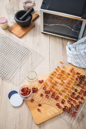 Dehydrate dried yellow and red tomatoes on stainless steel dehydrator tray and in glass jar for long term pantry in domestic kitchen on light wooden backgroundの写真素材