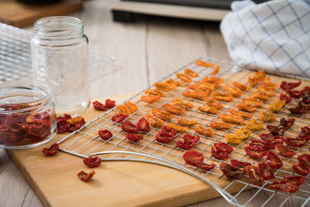 Dehydrate dried yellow and red tomatoes on stainless steel dehydrator tray and in glass jar for long term pantry in domestic kitchen on light wooden backgroundの写真素材