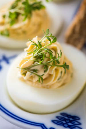Cold deviled eggs filled with cream cheese, cress, herbs and toast bread on blue white porcelain...