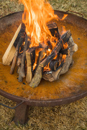 Fire of campire with well-seasoned logs of wood in metal fireplace bowl outside in garden on lawn
