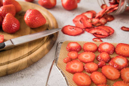 Fresh and dried strawberries from dehydrator for long term prepper pantry with knife, wooden cutting board and glass jar on light marble backgroundの写真素材
