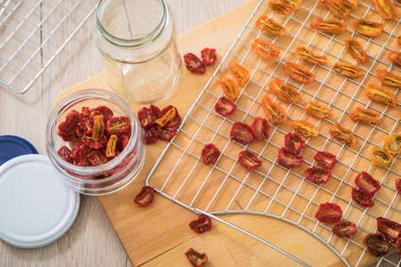Dehydrate dried yellow and red tomatoes on stainless steel dehydrator tray and in glass jar for long term pantry in domestic kitchen on light wooden backgroundの写真素材