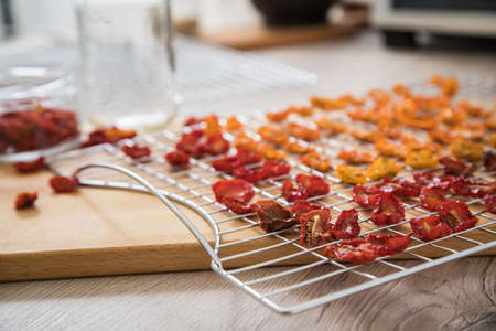Dehydrate dried yellow and red tomatoes on stainless steel dehydrator tray and in glass jar for long term pantry in domestic kitchen on light wooden backgroundの写真素材
