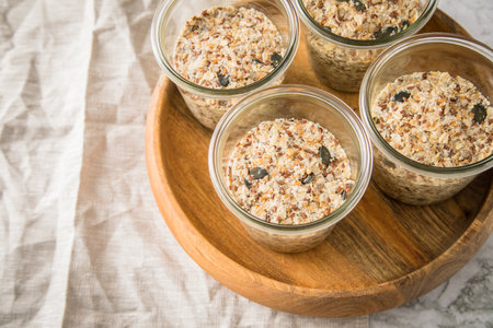 Raw dough of wholegrain bread with chia, oats, flaxseeds, sunflower and pumpkin seeds in glass jar for canning and prepper long term pantry on wooden tray, linen towel and light marble backgroundの写真素材