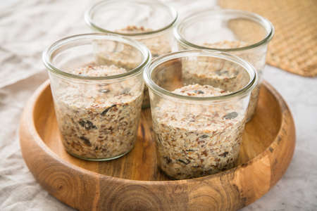 Raw dough of wholegrain bread with chia, oats, flaxseeds, sunflower and pumpkin seeds in glass jar for canning and prepper long term pantry on wooden tray, linen towel and light marble backgroundの写真素材