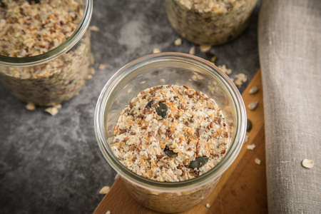 Raw dough of wholegrain bread with chia, oats, flaxseeds, sunflower and pumpkin seeds in glass jar for canning and prepper long term pantry on wooden board, linen towel and dark marble backgroundの写真素材