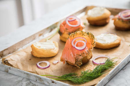 Gravlax a raw, marinated graved salmon with dill on bred roll bun with cream cheese, onion rings on tray with baking paper and light marble backgroundの写真素材