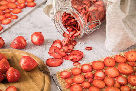 Fresh and dried strawberries from dehydrator for long term prepper pantry with knife, wooden cutting board and glass jar on light marble backgroundの写真素材