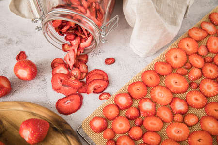 Fresh and dried strawberries from dehydrator for long term prepper pantry with knife, wooden cutting board and glass jar on light marble backgroundの写真素材