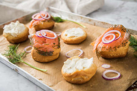 Gravlax a raw, marinated graved salmon with dill on bred roll bun with cream cheese, onion rings on tray with baking paper and light marble backgroundの写真素材