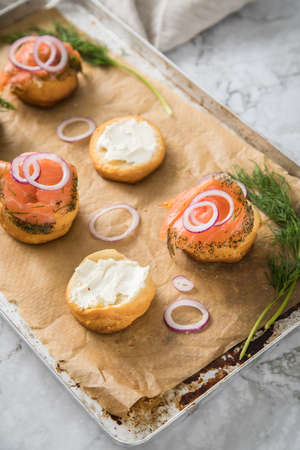 Gravlax a raw, marinated graved salmon with dill on bred roll bun with cream cheese, onion rings on tray with baking paper and light marble backgroundの写真素材