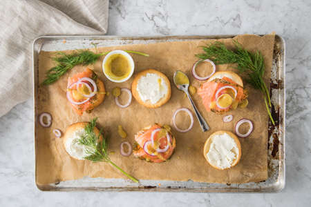 Gravlax a raw, marinated graved salmon with dill on bred roll bun with cream cheese, Scandinavian mustard sauce, onion rings on tray with baking paper and light marble backgroundの写真素材